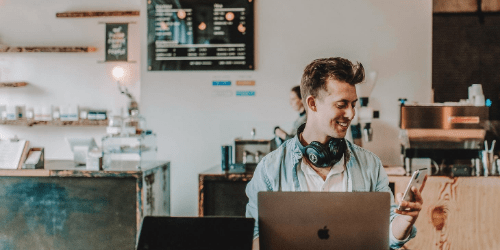 A smiling man with headphones behind a laptop.