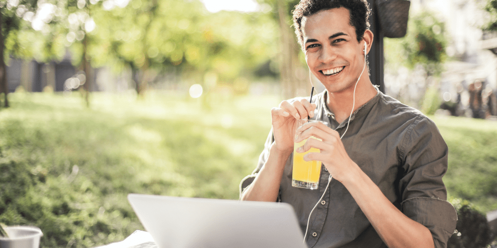 A man smiling in front of laptop with a beverage in his hand.