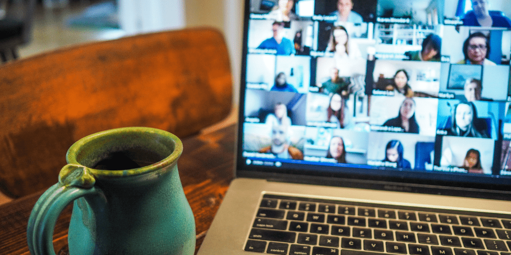 A coffee cup next to a laptop showing a video call with multiple participants.