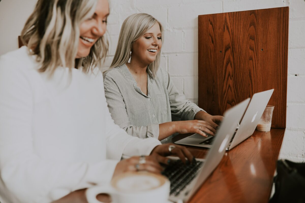 Two happy women with laptops talking.