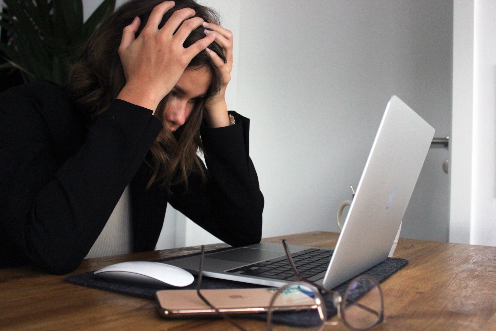 A woman in front of a laptop holding her head in frustration about outsourcing payroll.