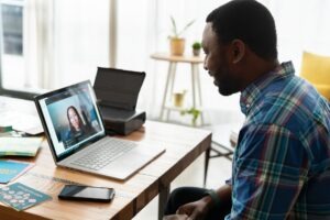A man communicating with a latino virtual assistants via video call on his laptop.