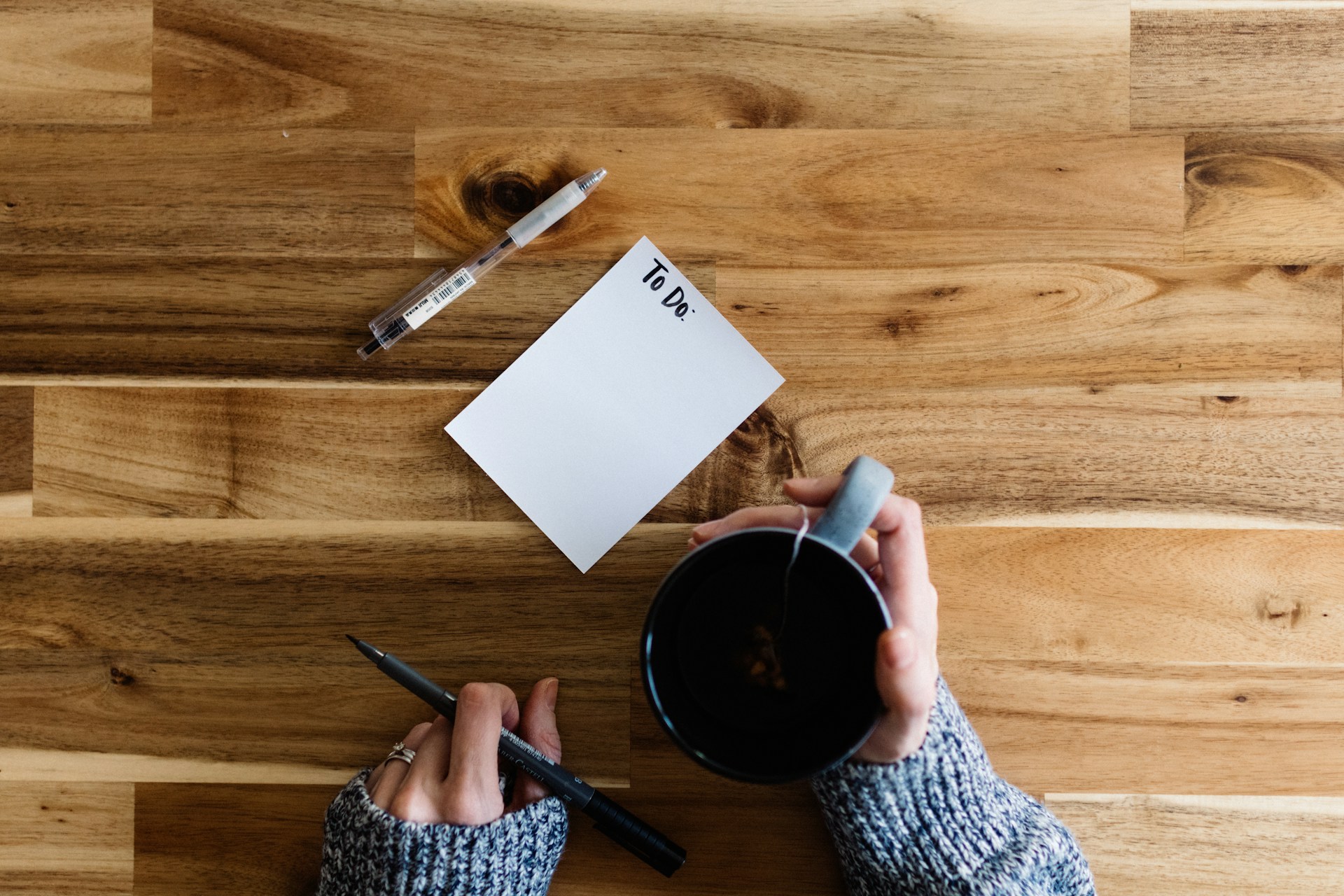 A woman with a cup of tea, two pens and a blank To Do List on the table in front of her.