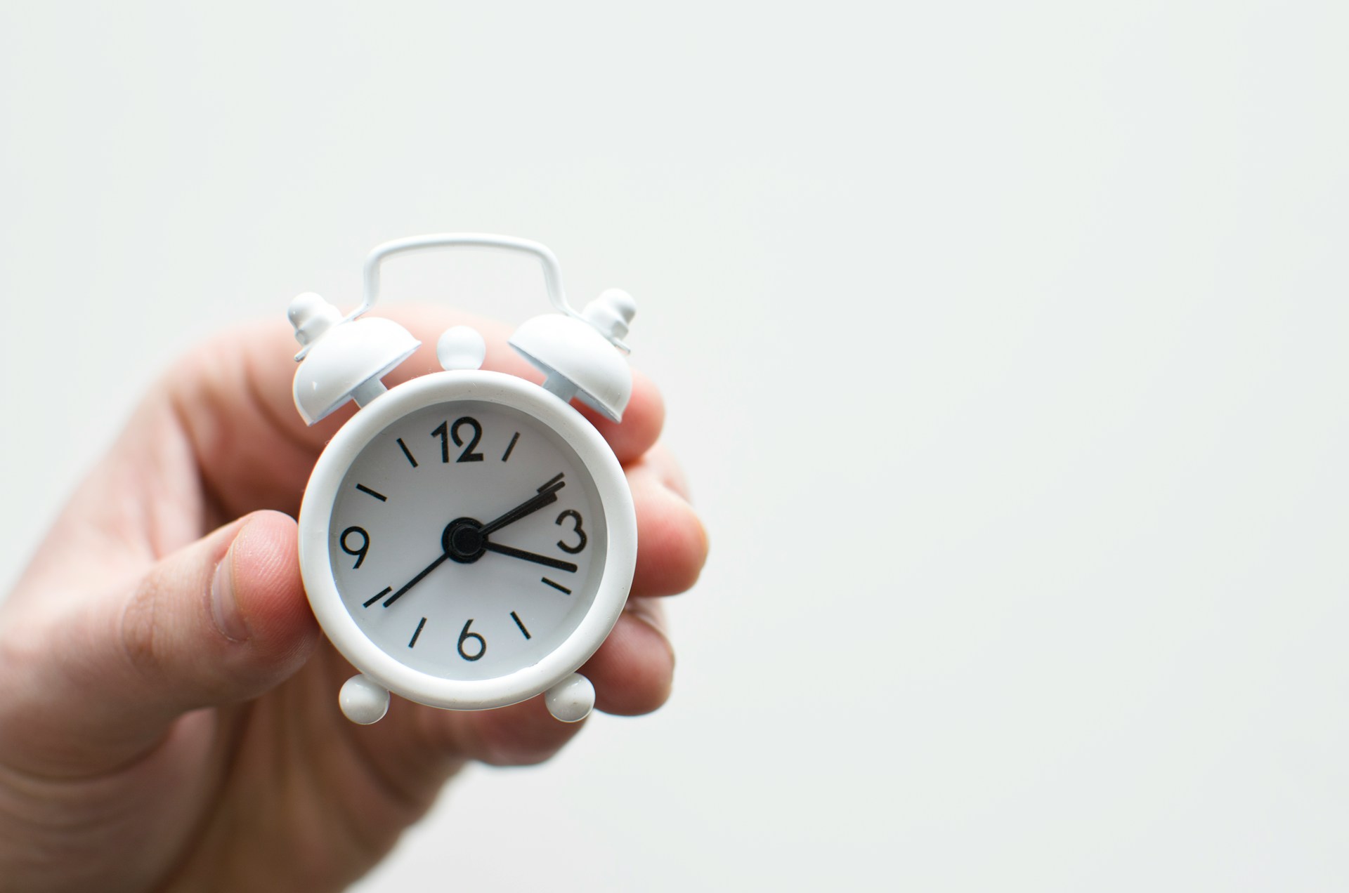 A hand holding a tiny, white alarm clock with the time set to 2:18. executive assistant daily checklist