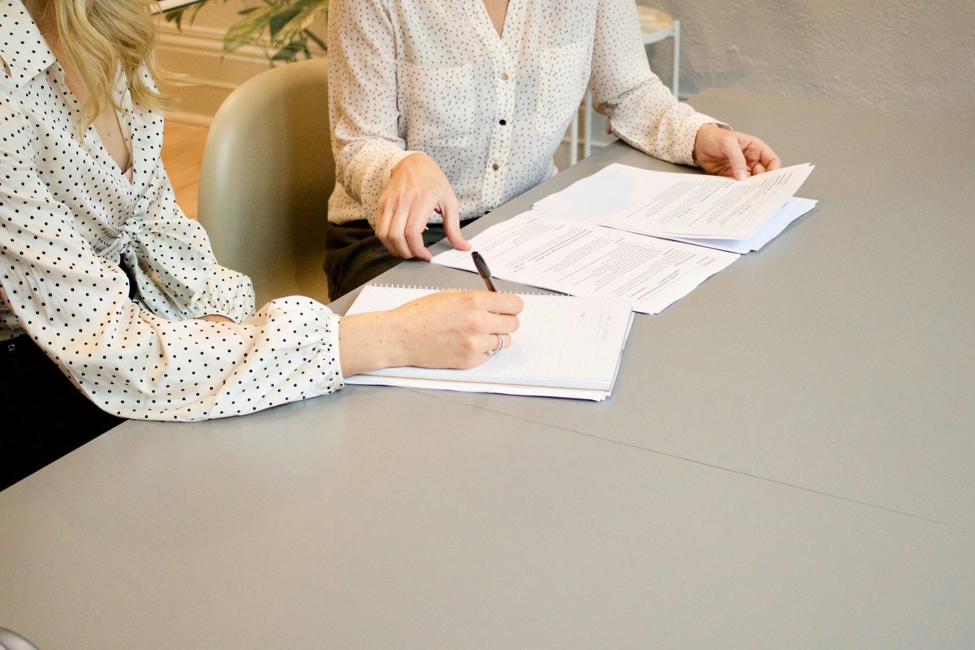 A woman signing a freelancer contract while another woman helps her.