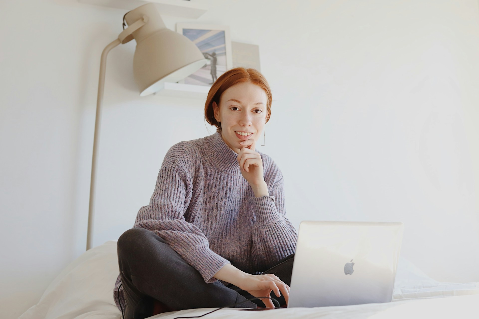 A smiling woman sitting on a bed with a laptop.